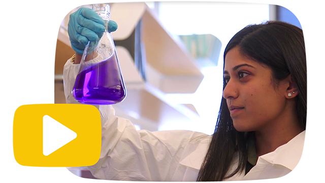This image shows a woman holding up a beaker of fluid. The image clicks to an external video about Rowan University's transformation.