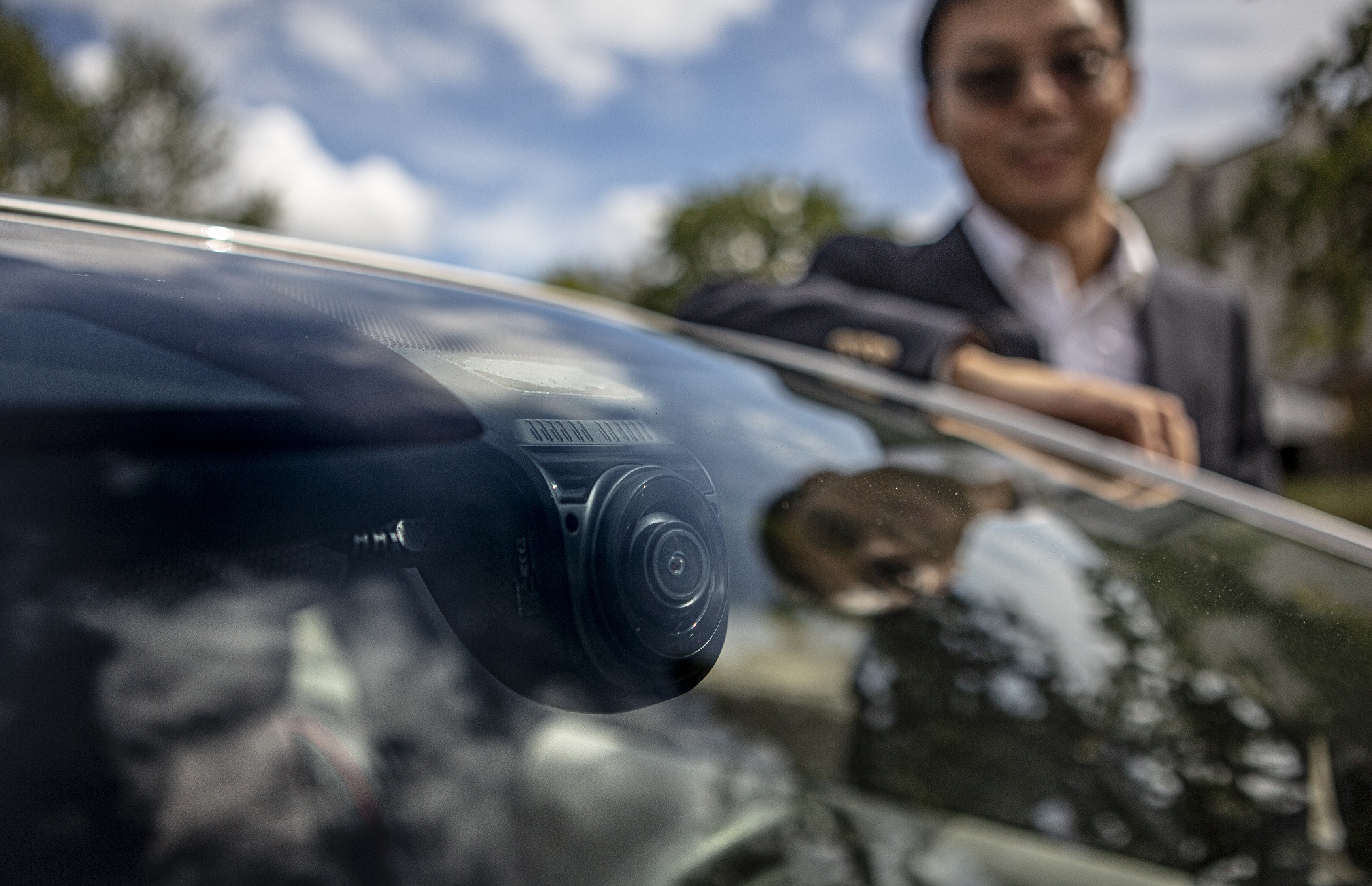 In the foreground, looking into a car's windshield, we see a camera mounted just below the rear-view mirror, aimed at the driver. In the background, Dr. Ning Wang stands smiling while standing by the driver's side door of a small silver sedan. 