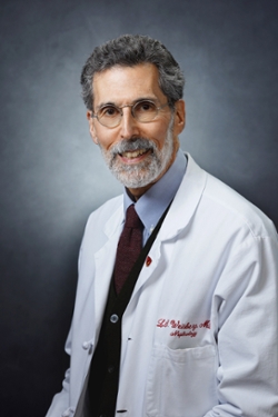 This is a professional portrait of Lawrence Weisberg, MD, an older white man wearing a white doctor's coat. 