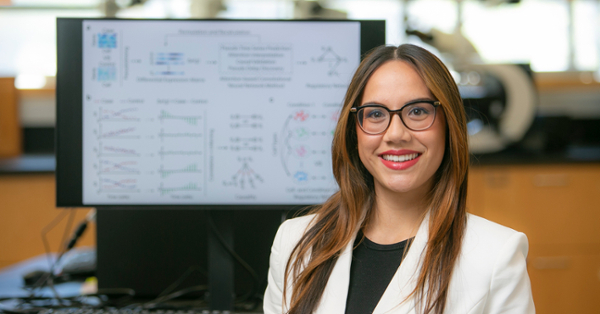 Madison Dautle stands in front of a presentation screen displaying various mathematical and algorithmic diagrams.