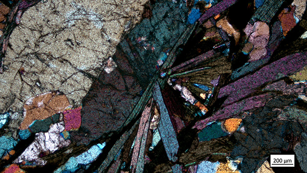 A colorful microscopic image of a thin piece of rock shows mineral deposits that appear in the shape of a butterfly. 