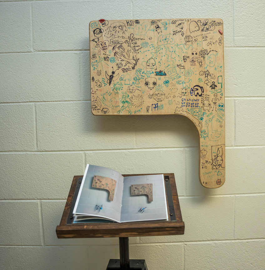 "Group Project" - a carved wooden school desk with graffiti sketches all over it