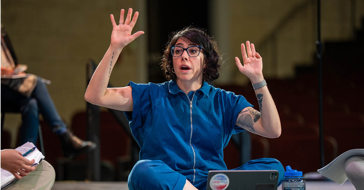 Rachel Chavkin sits on Tohill Stage, arms raised during demonstration with theatre majors