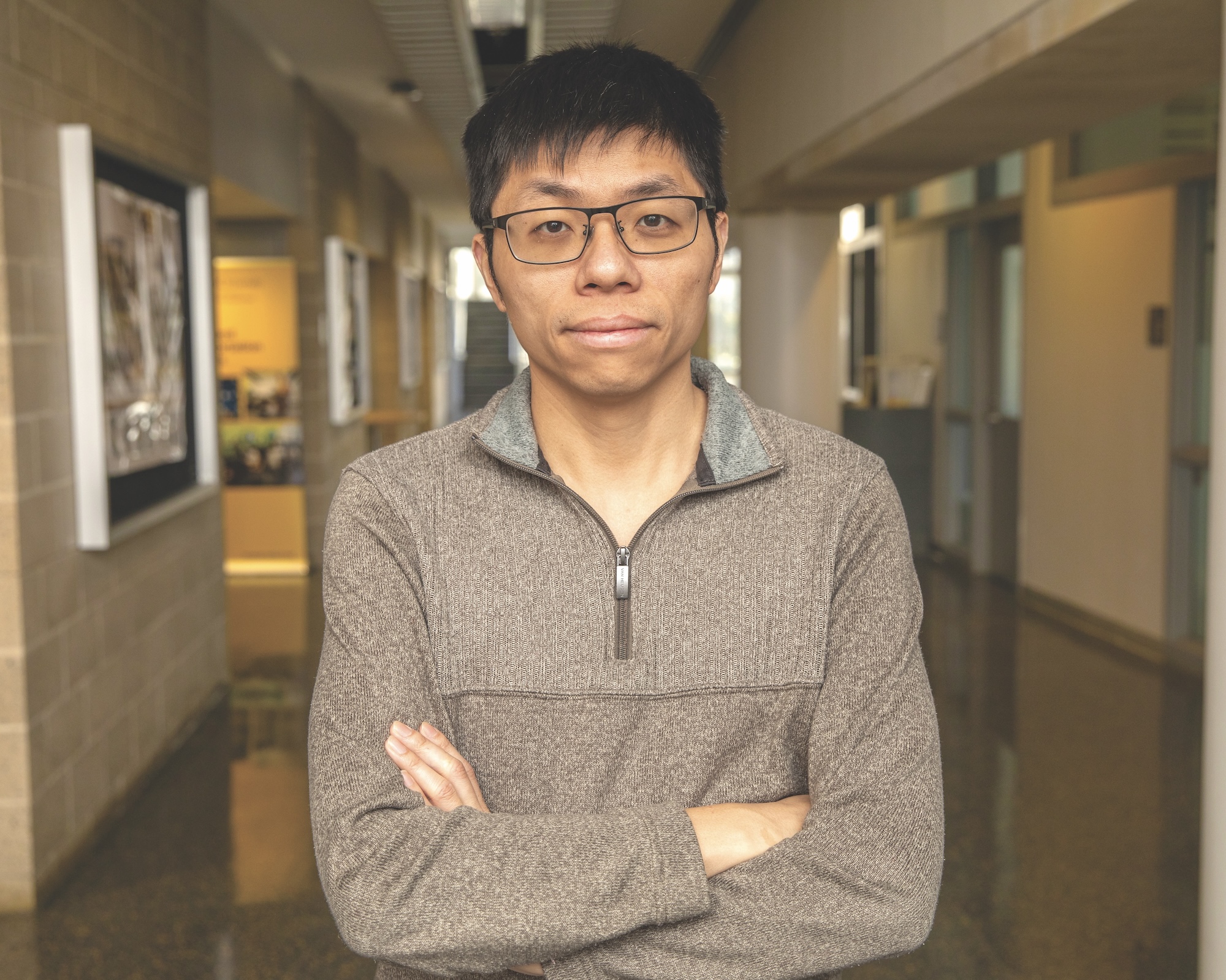Chen Shen stands in a hallway with his arms crossed.