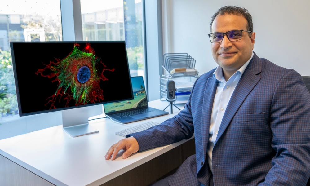 Mohamed Abouelkhair seated at a desk beside a computer displaying a microscope image in a laboratory office.