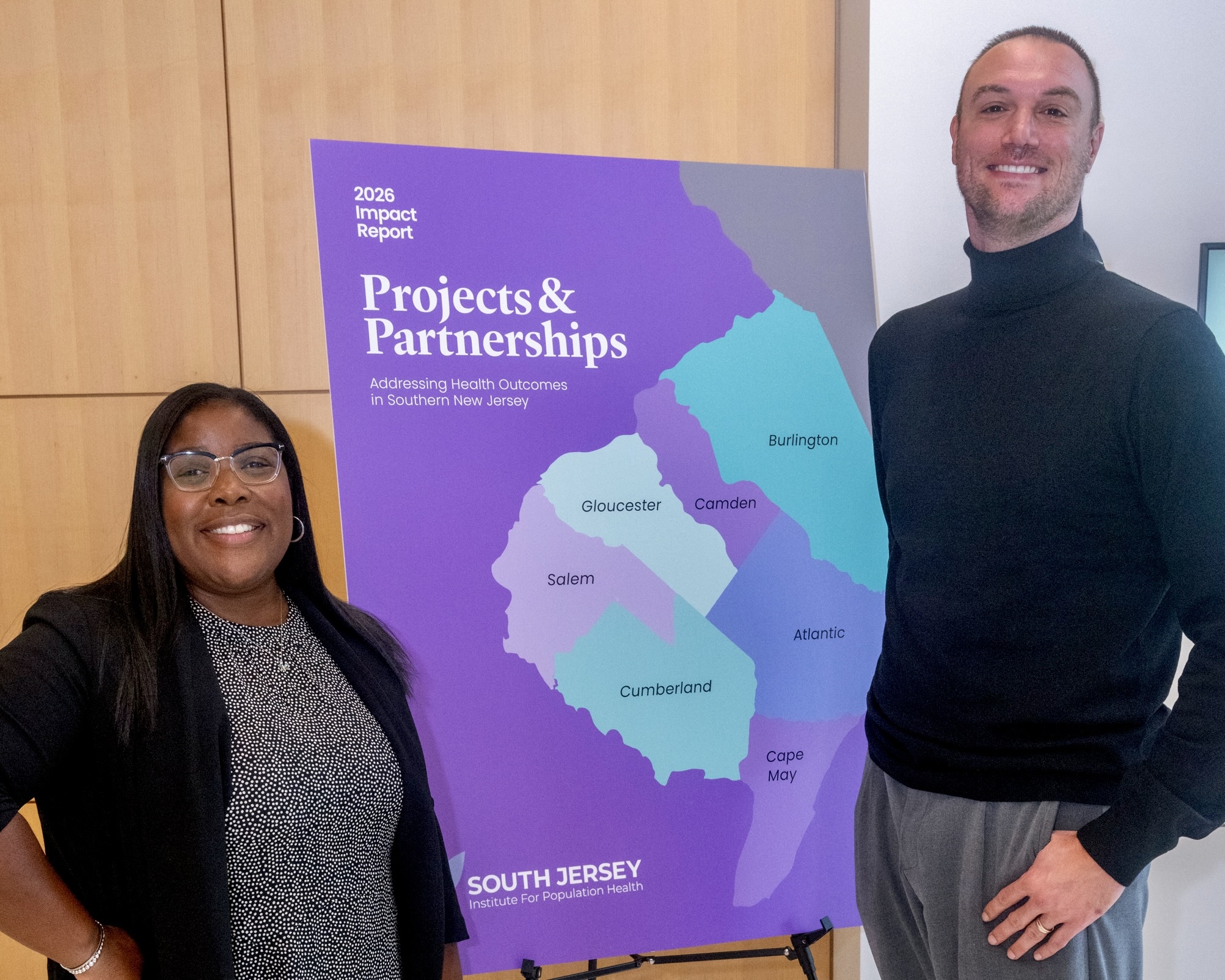 Nicole Vaughn and Stephen Danley stand alongside a display of the South Jersey Institute for Population Health's 2026 Impact Report.