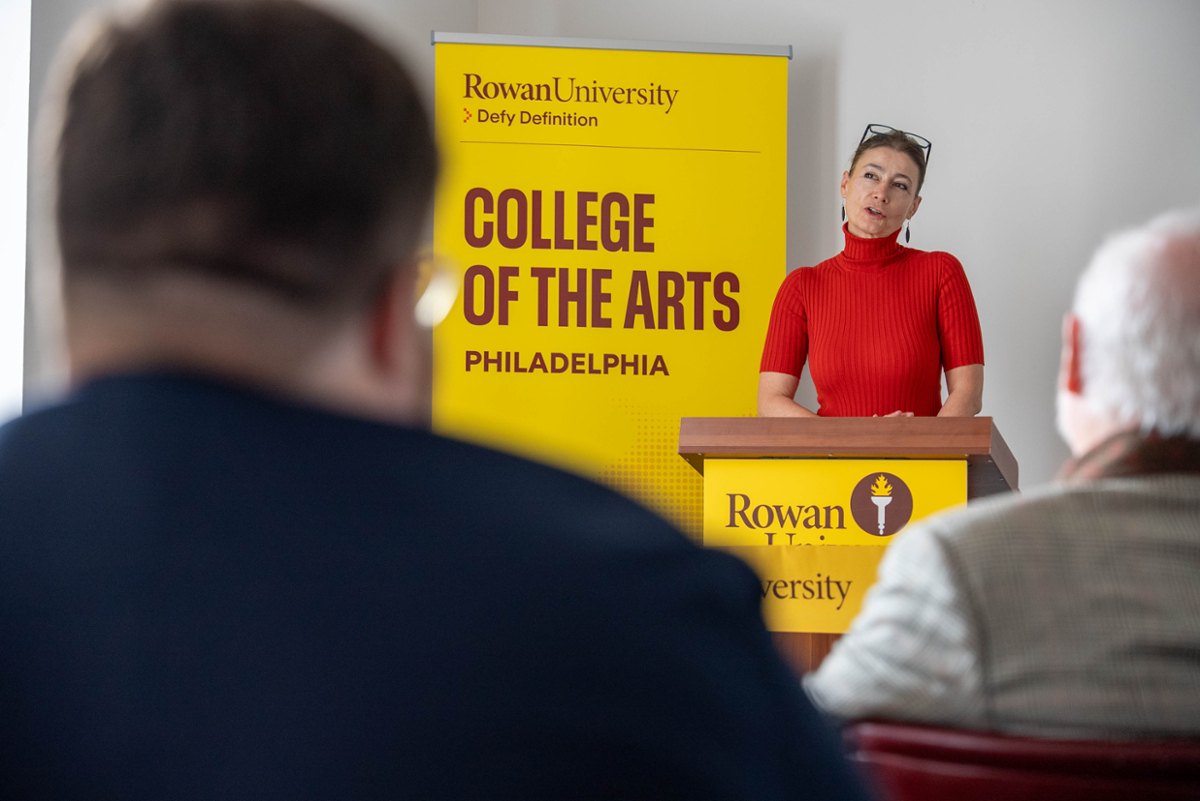 Provost Voki Pophristic stands behind a podium next to a tall banner that reads "College of the Arts Philadelphia"
